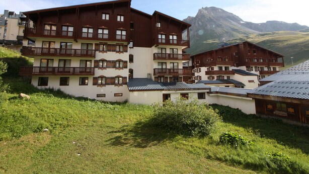 Un edificio de varios pisos con balcones, frente a un paisaje montañoso.