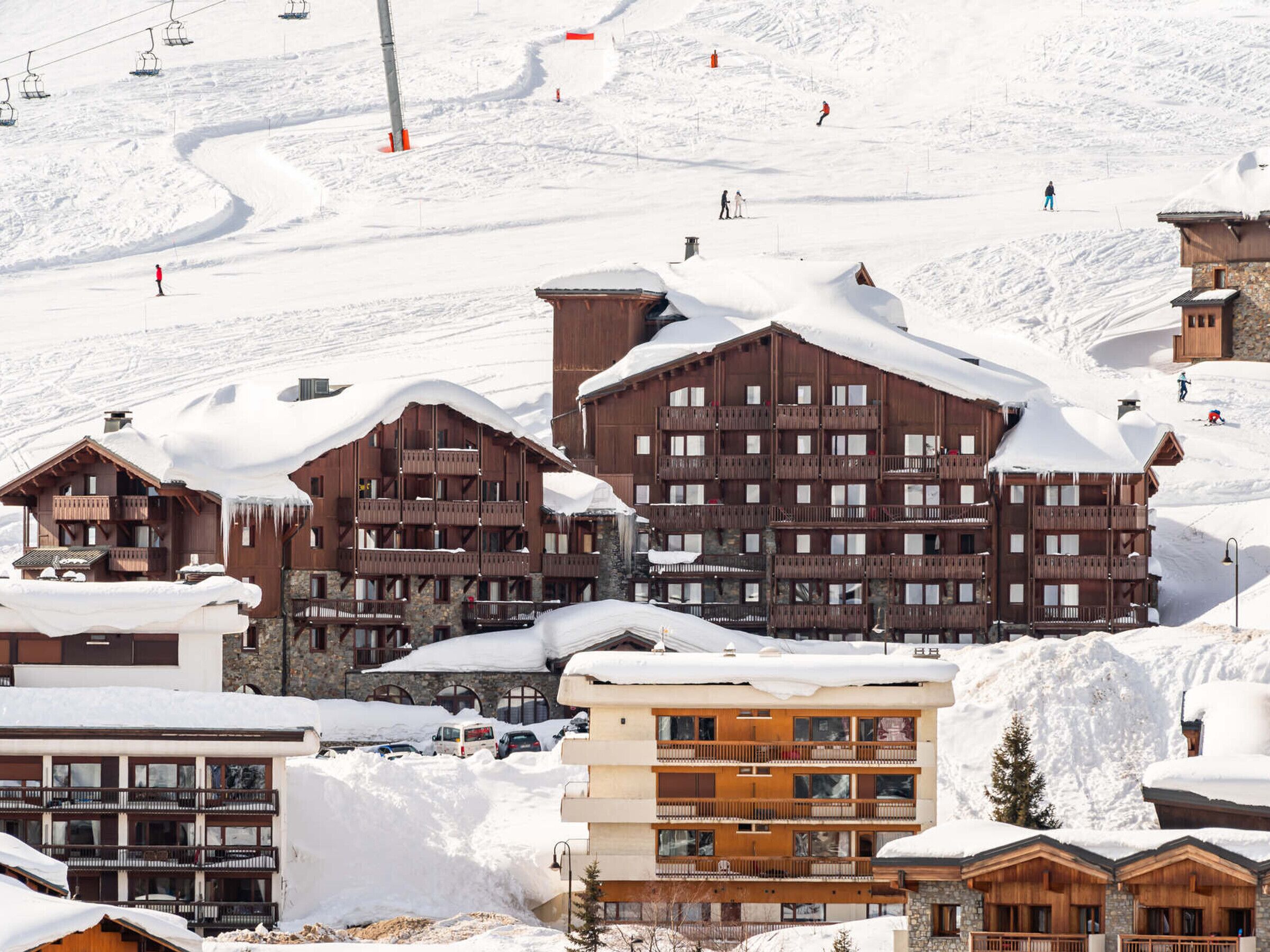 Een bergresort bedekt met sneeuw, met houten gebouwen, skiliften en skiërs.