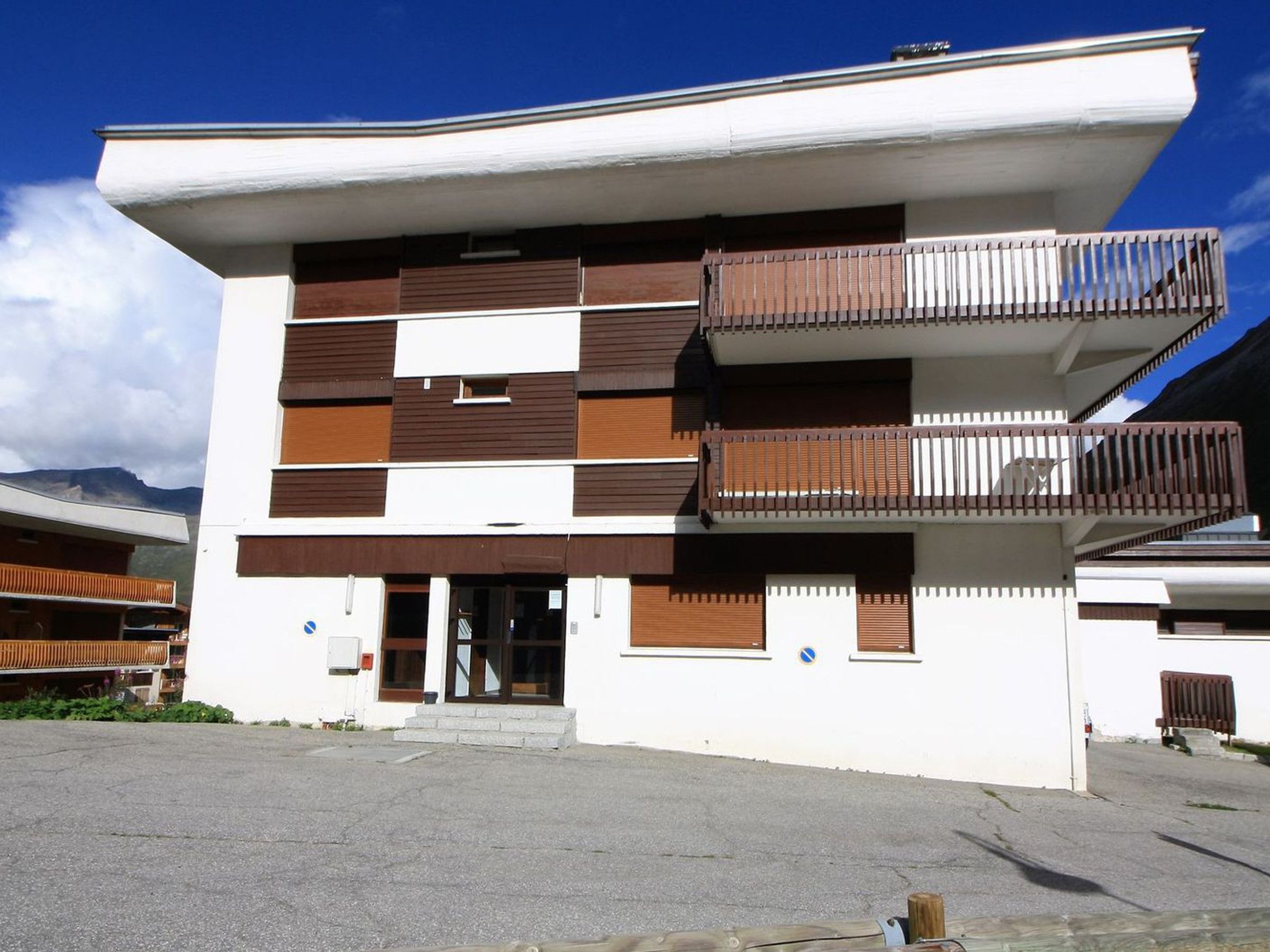 A modern building with a flat roof, multiple balconies, and a central entrance.