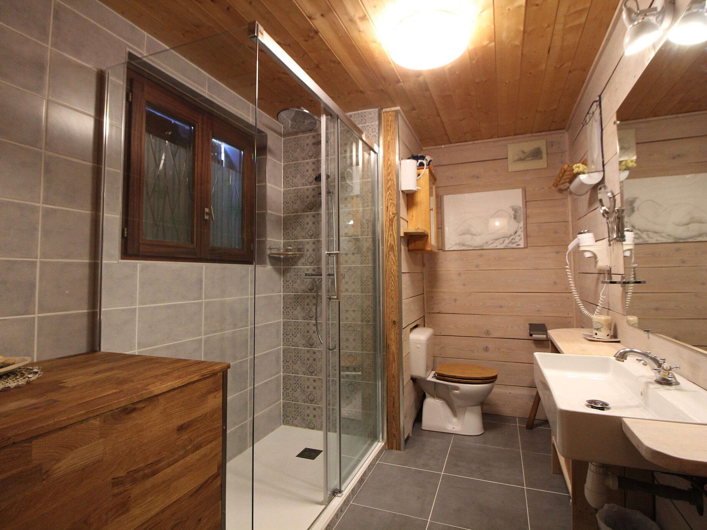 Een badkamer met een houten wastafelmeubel, een douchecabine van glas, een toilet en een wastafel met spiegel.