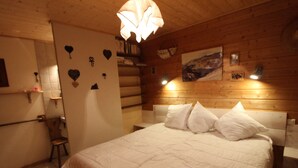 Una camera da letto con una testiera in legno, un letto grande con biancheria bianca, un pavimento in legno e un lampadario fissato al muro.