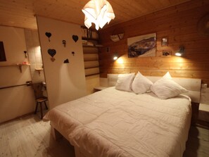 A bedroom with a wooden headboard, a large bed with white bedding, a wooden floor, and a wall-mounted light fixture. - Traditional wooden chalet, cozy, 3 bedrooms, 8 people, south balcony (Tignes)