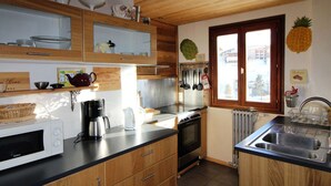 Cucina con mobili in legno, forno a microonde, macchina da caffè e finestra con vista esterna.