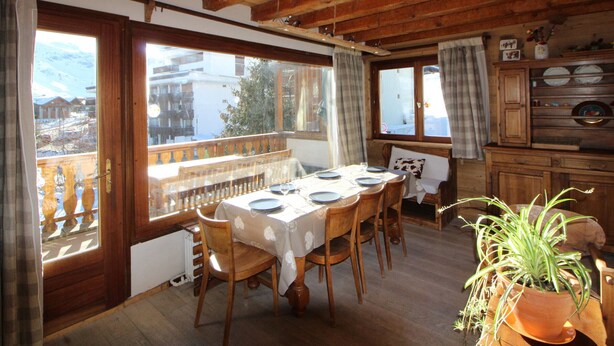 Zona pranzo con tavolo in legno apparecchiata per quattro persone, una panca e vista su un paesaggio innevato attraverso ampie finestre.