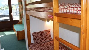 A bunk bed with a patterned mattress, a wooden bench, and a window with curtains. - Cozy studio 4 ppl, south balcony, Tignes center (Tignes-Le Lavachet)