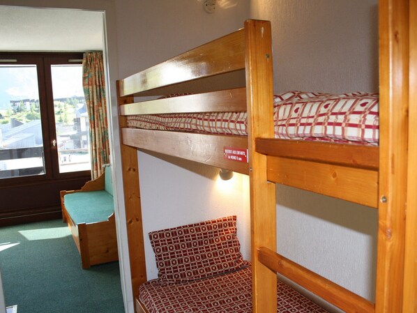 A bunk bed with a patterned mattress, a wooden bench, and a window with curtains.
