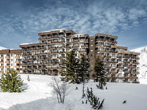 A multi-story hotel with balconies, set against a snowy mountain backdrop.