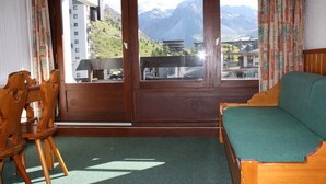A room with a wooden sofa and chairs, a balcony with a view of mountains and buildings. - Cozy studio 4 ppl, south balcony, Tignes center (Tignes-Le Lavachet)