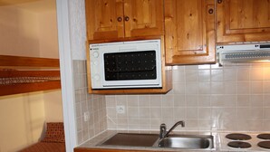 A compact kitchen with wooden cabinets, a built-in microwave, a sink, and a dishwasher. - Cozy studio 4 ppl, south balcony, Tignes center (Tignes-Le Lavachet)