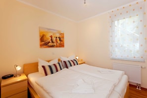 A hotel room with a large bed, a nightstand with a lamp, a painting on the wall, and a window with curtains.