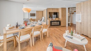 A modern living room with a wooden dining table, comfortable seating, a built-in TV, and a fireplace. - Modern Apartment 3* Tignes - 80m² - 8 people (Tignes)