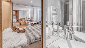 A modern hotel room with a large bed, a cozy reading nook, a dining area, and a contemporary bathroom with a glass shower enclosure. - Modern Apartment 3* Tignes - 80m² - 8 people (Tignes)
