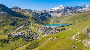 Un paysage montagneux avec une ville nichée dans une vallée, agrémenté d’un lac et de sommets enneigés en arrière-plan.