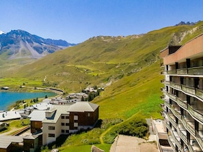 A mountainous landscape with a lake, a modern building with balconies, and traditional houses.