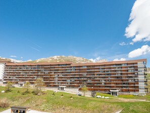 A multi-story hotel with balconies, a small garden area, and a mountainous backdrop. - Apartment in Tignes, Lake and Mountain View, Sleeps 6 (Tignes)