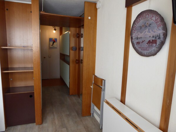 Un couloir étroit avec des portes en bois et un mur blanc. Une échelle métallique est appuyée contre le mur.