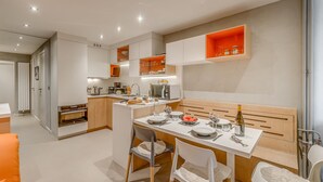 A modern kitchen with white cabinetry, a central island, and orange accents. - Renovated 1BR 4 pers in Tignes, south balcony (Tignes-Le Lavachet)