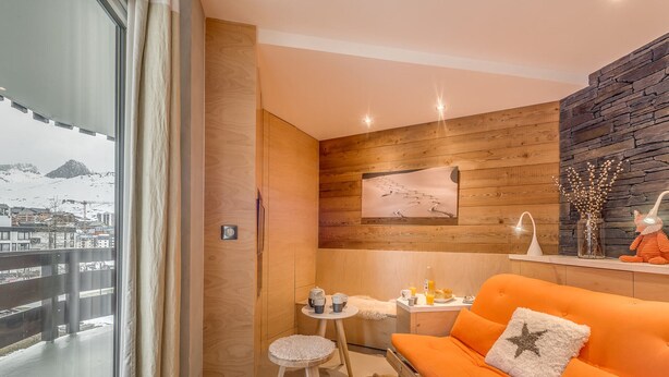 A modern living room with a wooden wall, a sofa, a small table, and a view of a snowy mountain. - Renovated 1BR 4 pers in Tignes, south balcony (Tignes-Le Lavachet)