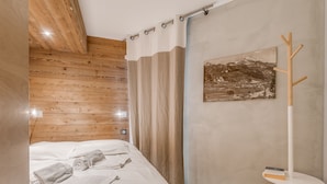 A bedroom with a wooden ceiling, a bed with white linens, a coat rack, and a painting on the wall. - Renovated 1BR 4 pers in Tignes, south balcony (Tignes-Le Lavachet)