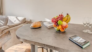 A dining table with a fruit bowl, a loaf of bread, a book, and wine glasses.
