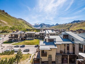 A modern hotel with a mountain view, featuring a mix of traditional and contemporary architecture, a parking area, and a clear sky.