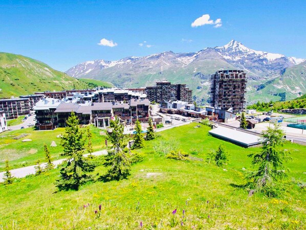 A modern hotel complex with multiple buildings, a parking area, and a mountainous backdrop.