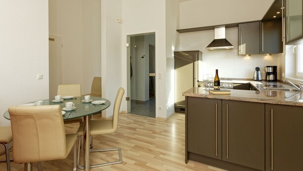 Een moderne keuken met een centraal eiland, roestvrijstalen apparatuur en een eethoek met een glazen tafel en stoelen.