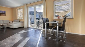 A modern living room with a sofa, a dining table with chairs, and a view through glass doors to an outdoor area.