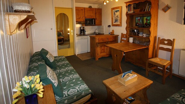 A cozy living room with a green patterned sofa, wooden dining table, and chairs. A small wooden cabinet with a television is in the background. - Cozy Studio 4 pax in Tignes (Tignes-Le Lavachet)