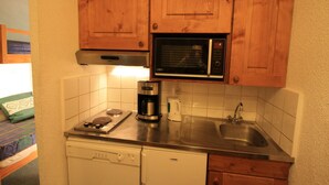 A compact kitchen with wooden cabinets, a microwave, a coffee maker, and a dishwasher. - Cozy Studio 4 pax in Tignes (Tignes-Le Lavachet)