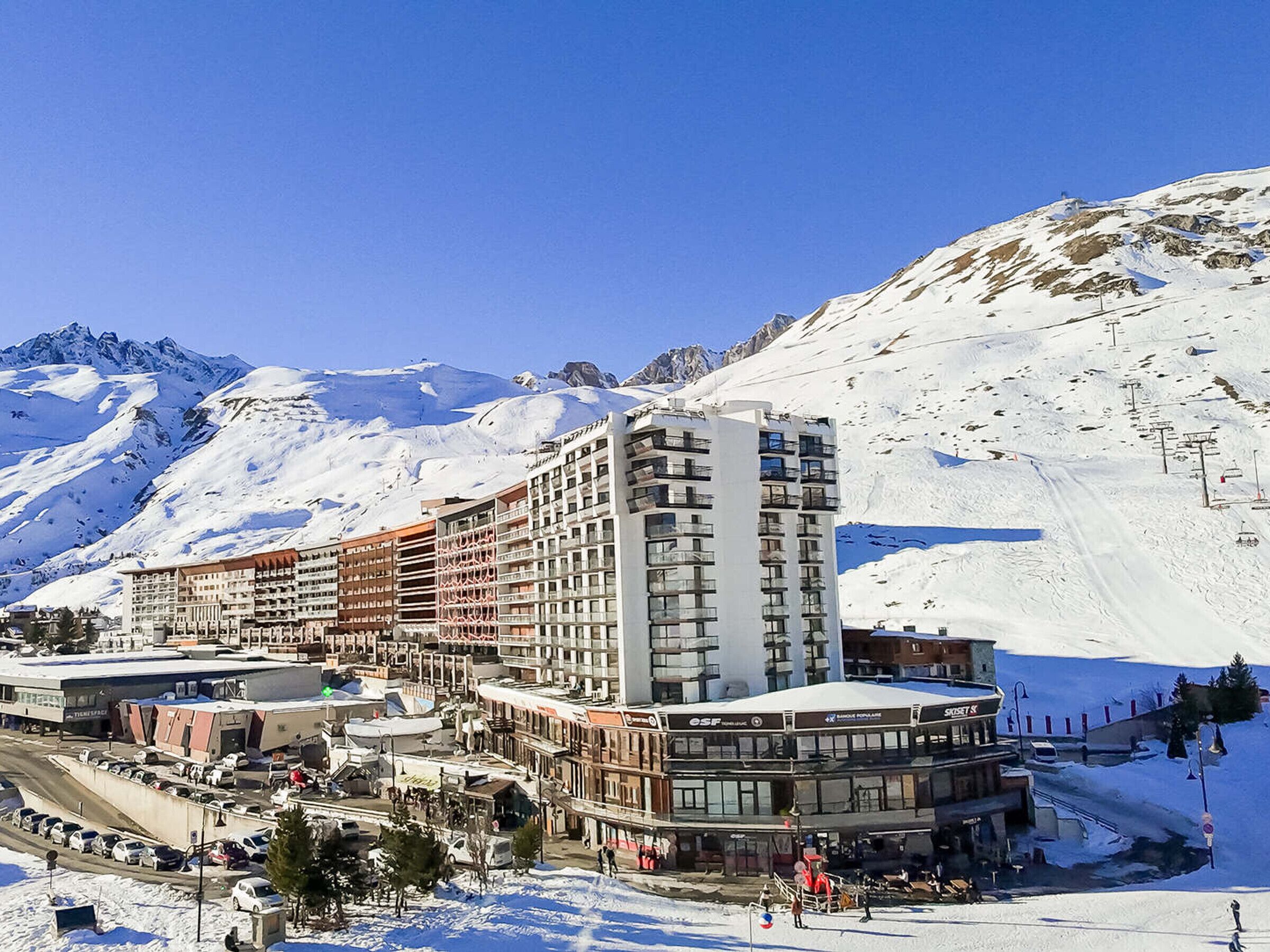 A multi-story hotel with a ski lift in the background, surrounded by snow-covered mountains.