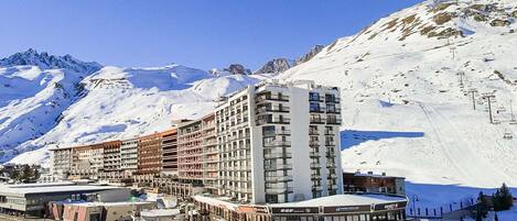 A multi-story hotel with a ski lift in the background, surrounded by snow-covered mountains.