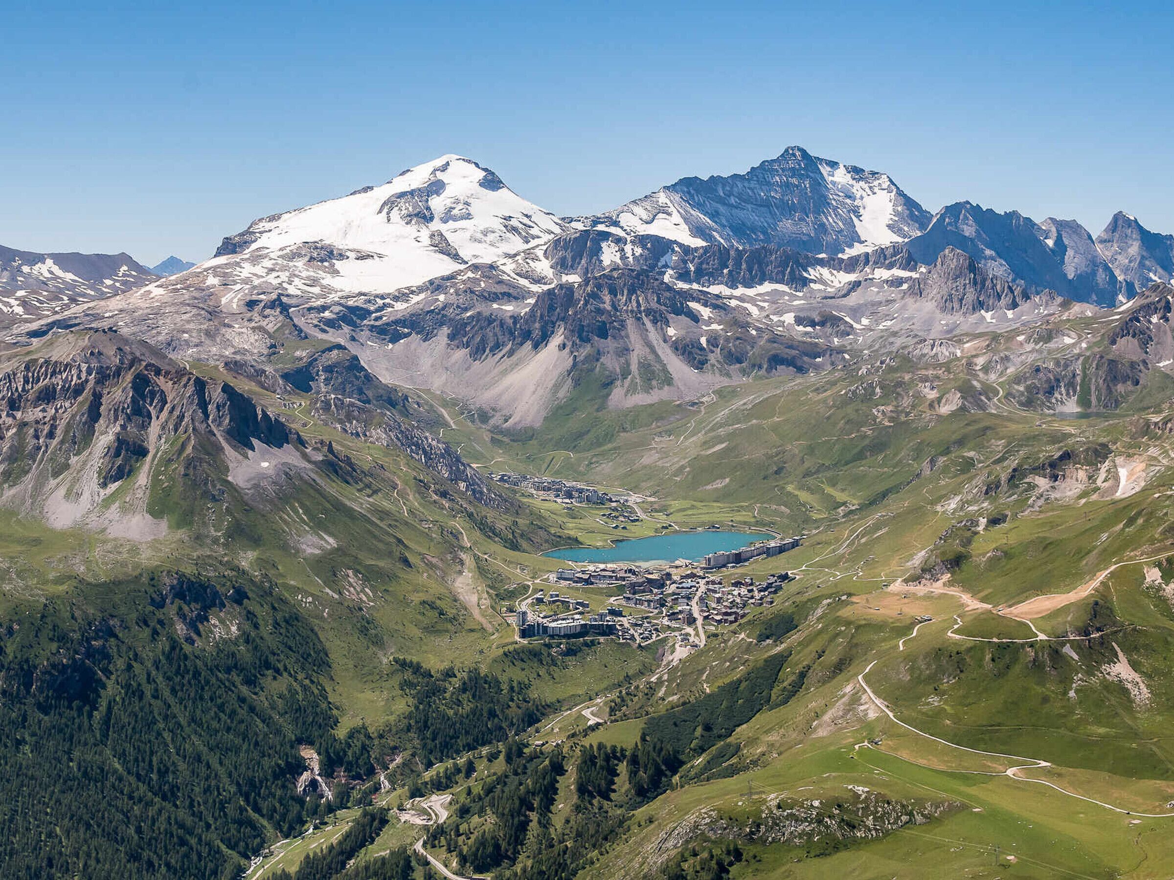 Eine Berglandschaft mit einem See, einer kleinen Siedlung und einem markanten, schneebedeckten Gipfel.