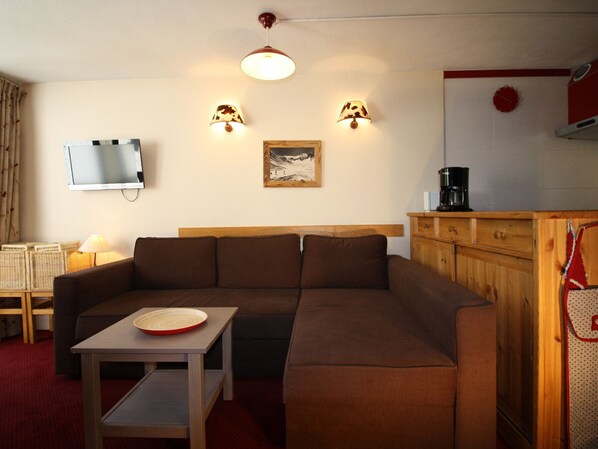 Kodikas olohuone, jossa on sohva, pieni pöytä, televisio, seinälle asennetut lamput ja taulu.