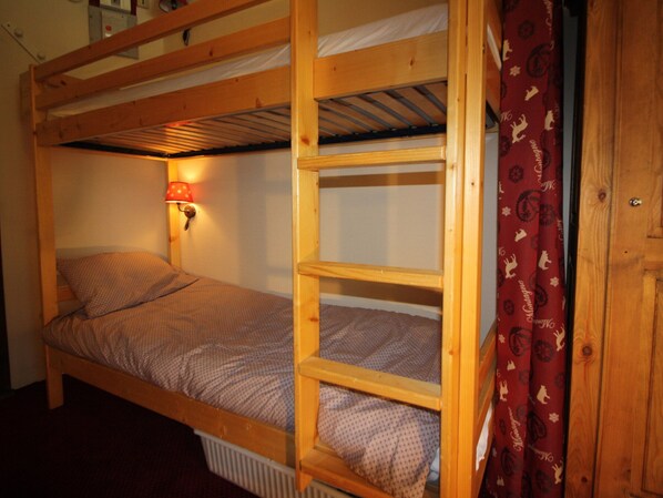 A bunk bed with a red lamp on the left side, a wooden ladder, and a red curtain with a pattern.