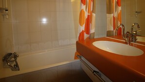 A bathroom with a bathtub, a sink with a mirror, and orange and white patterned curtains. - Cozy 4-person studio with lake view balcony (Tignes)