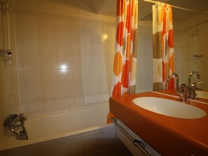 A bathroom with a bathtub, a sink with a mirror, and orange and white patterned curtains.