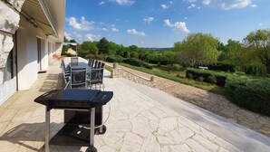 Un patio exterior con una parrilla, sillas y vistas al campo.