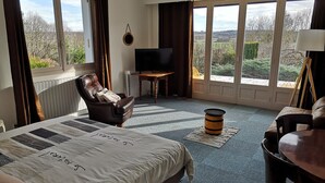 Habitación de hotel con una cama grande, un sillón de cuero, un televisor y vistas al exterior.