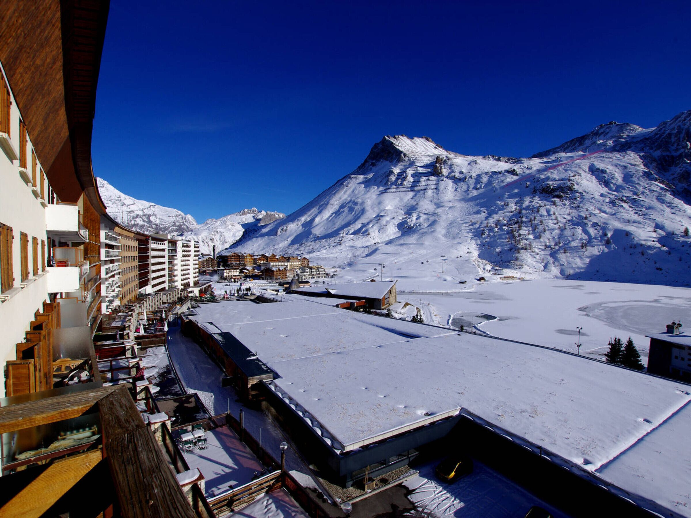 Ein schneebedeckter Berg mit einem Skiort im Vordergrund, mit Gebäuden mit Balkonen und einer Seilbahn.