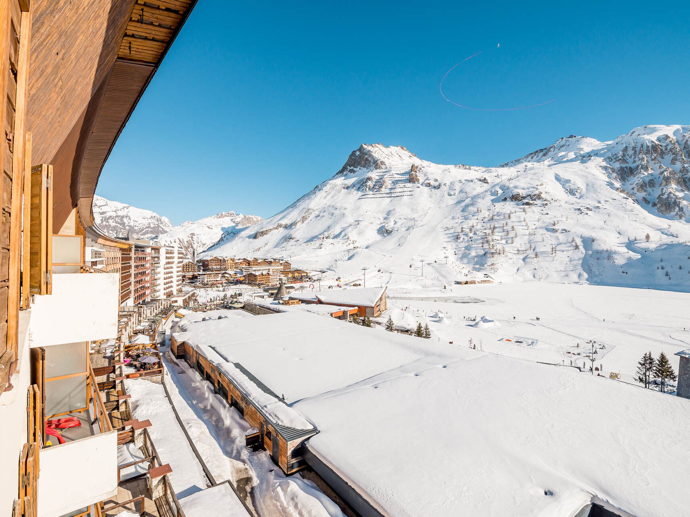 A snow-covered mountain landscape with a ski resort, wooden buildings, and a clear sky.