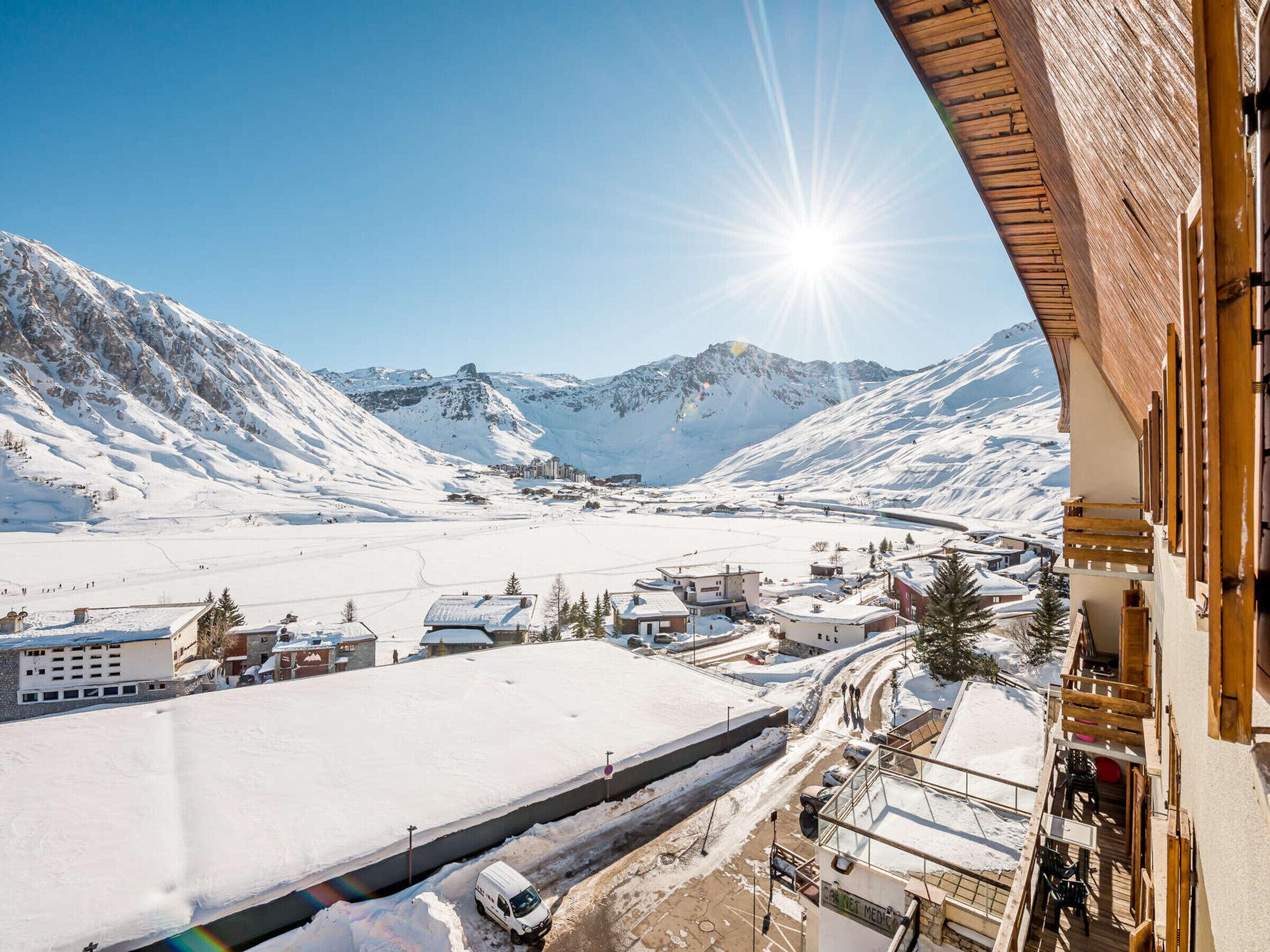 A snow-covered mountain landscape with a clear sky, a road with a vehicle, and buildings with balconies.