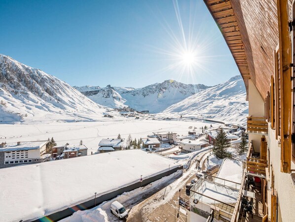 A snow-covered mountain landscape with a clear sky, a road with a vehicle, and buildings with balconies. - Comfortable family apartment, 7 people, lake view in Tignes (Tignes)