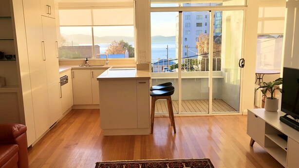 Una cocina moderna con un ventanal grande, una zona de comedor con sofá rojo y un balcón con vistas a la ciudad.