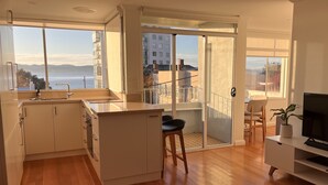 Una cocina moderna con un amplio ventanal, un balcón con vista al mar y un televisor sobre un mueble.