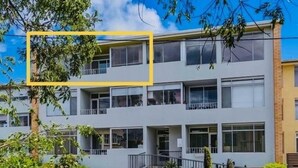 Un edificio residencial de varios pisos con balcones, una entrada central y zonas verdes aledañas.