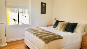Un dormitorio con una cama grande, una ventana, un radiador y una mesita de noche pequeña.