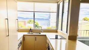 Una cocina moderna con un amplio ventanal, un fregadero y vistas a un paisaje urbano y montañas.