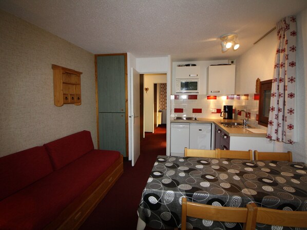 A compact room with a kitchenette, a red sofa, and a dining table with chairs.