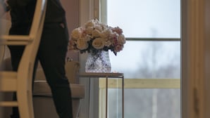 A room with a wooden floor, a white chair, a small table with a vase of flowers, and a door leading to a balcony. - Tokeryds Herrgård (Jonkoping)